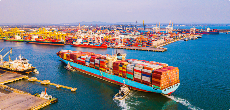 A colorful ship loaded with containers enters a shipping harbor.