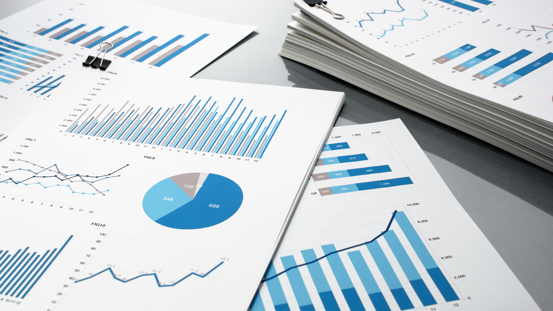Blue graphs and charts. Business reports and pile of documents on gray reflection background.