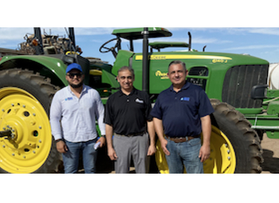 Three men standing in front of a large green tractor