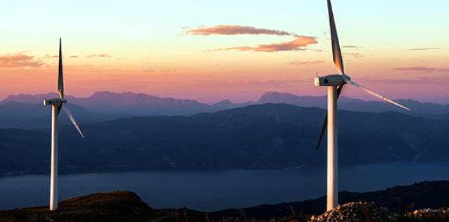 Two windmills at sunset are in the foreground with hills mountain and a river in the background