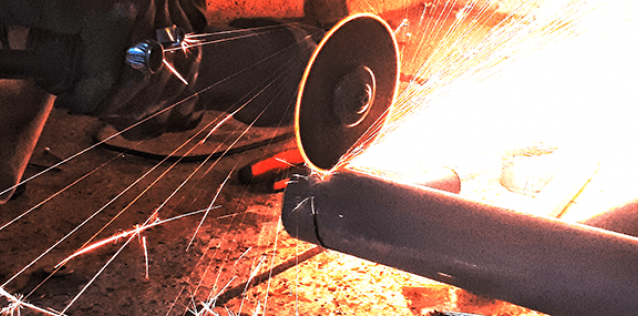 close up of person grinding steel pipe and emiting sparks