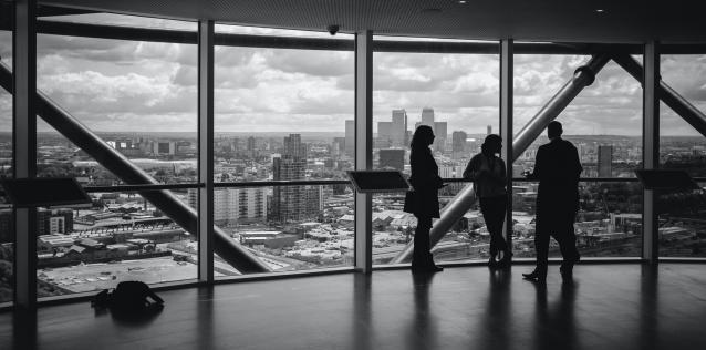 There persons having a discussion in front of a large window looking out on a city skyline