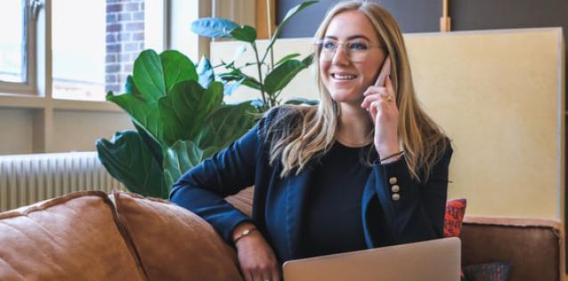 Young woman with glasses sitting on a couch and talking on a phone