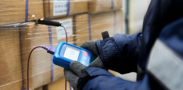 Hand of worker using a thermometer to measure the temperature of goods in cargo boxes