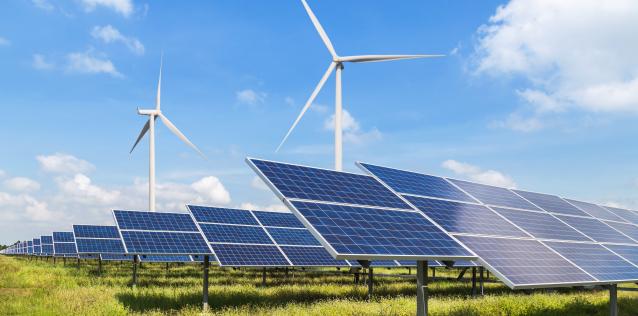 Field with solar panels and windmills against a blue sky with fluffy clouds