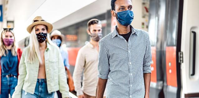 Crowd of people walking at railroad station platform covered by protective face mask