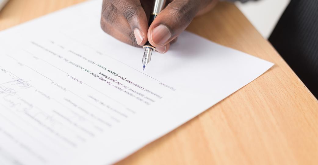 Hand holding a pencil filling out a form on a desk